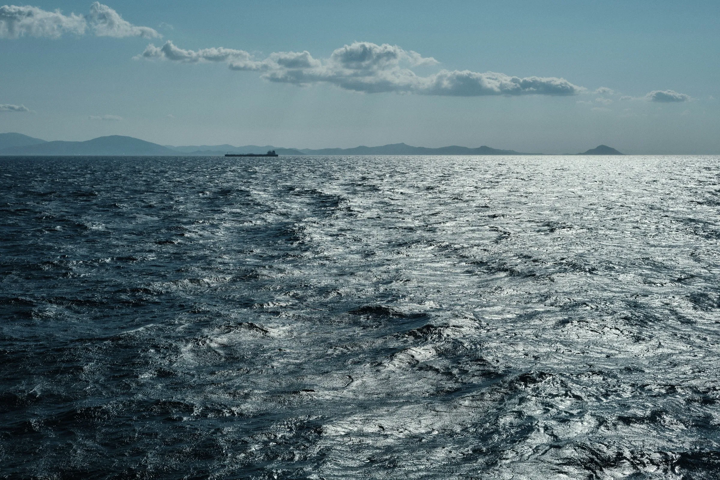 Wind-roughened open sea with distant islands under a bright sky