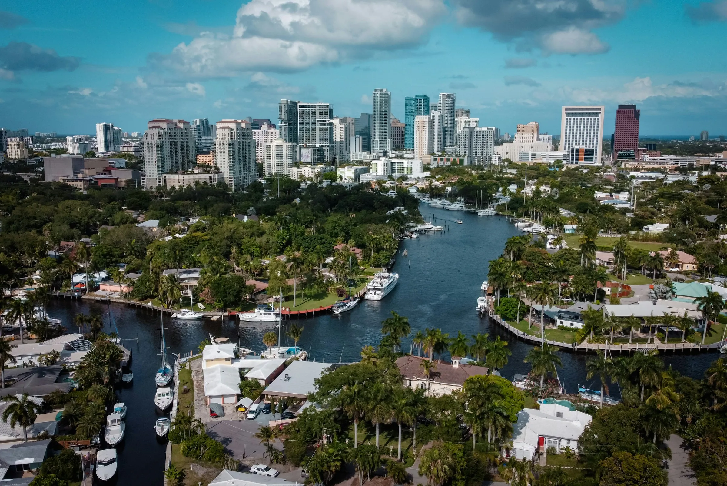 Aerial view of a river winding through Fort Lauderdale, boats moored along both banks beneath the downtown skyline