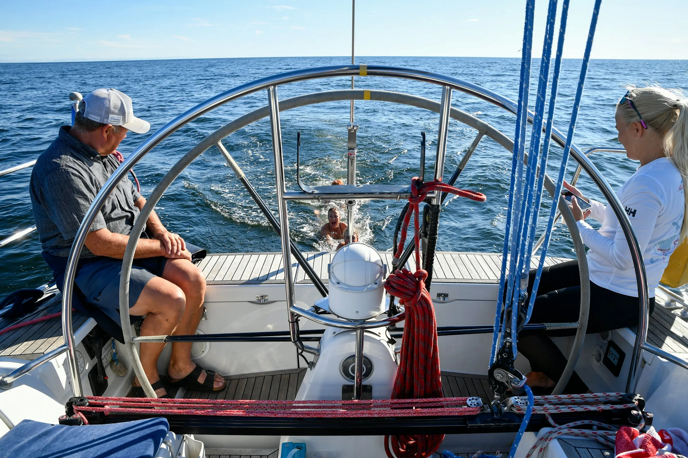 Two people in the cockpit of a sailing yacht under way, one at the wheel