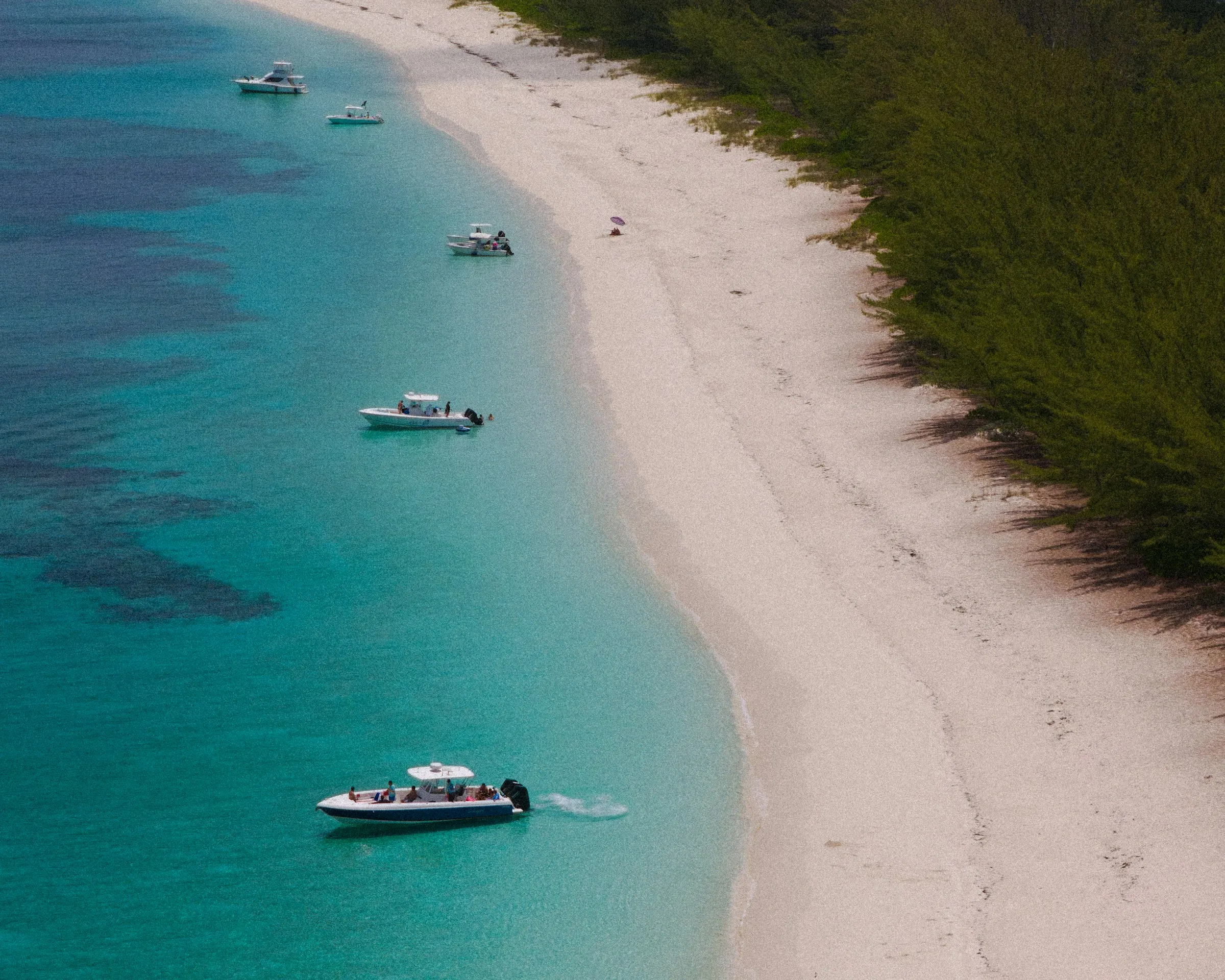 Boats dot a beautiful beach with turquoise waters.