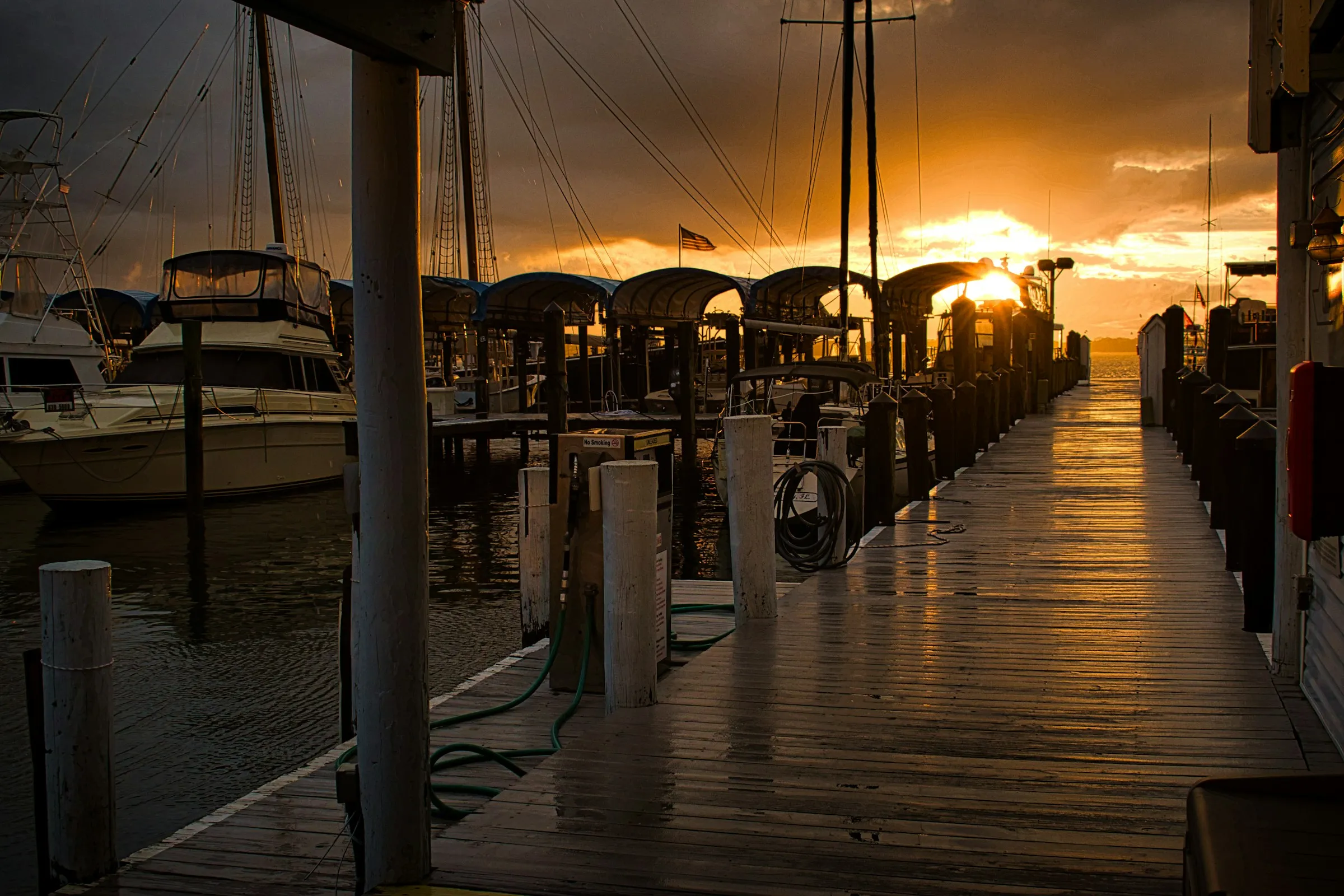 Wooden dock between covered slips and moored boats at sunset