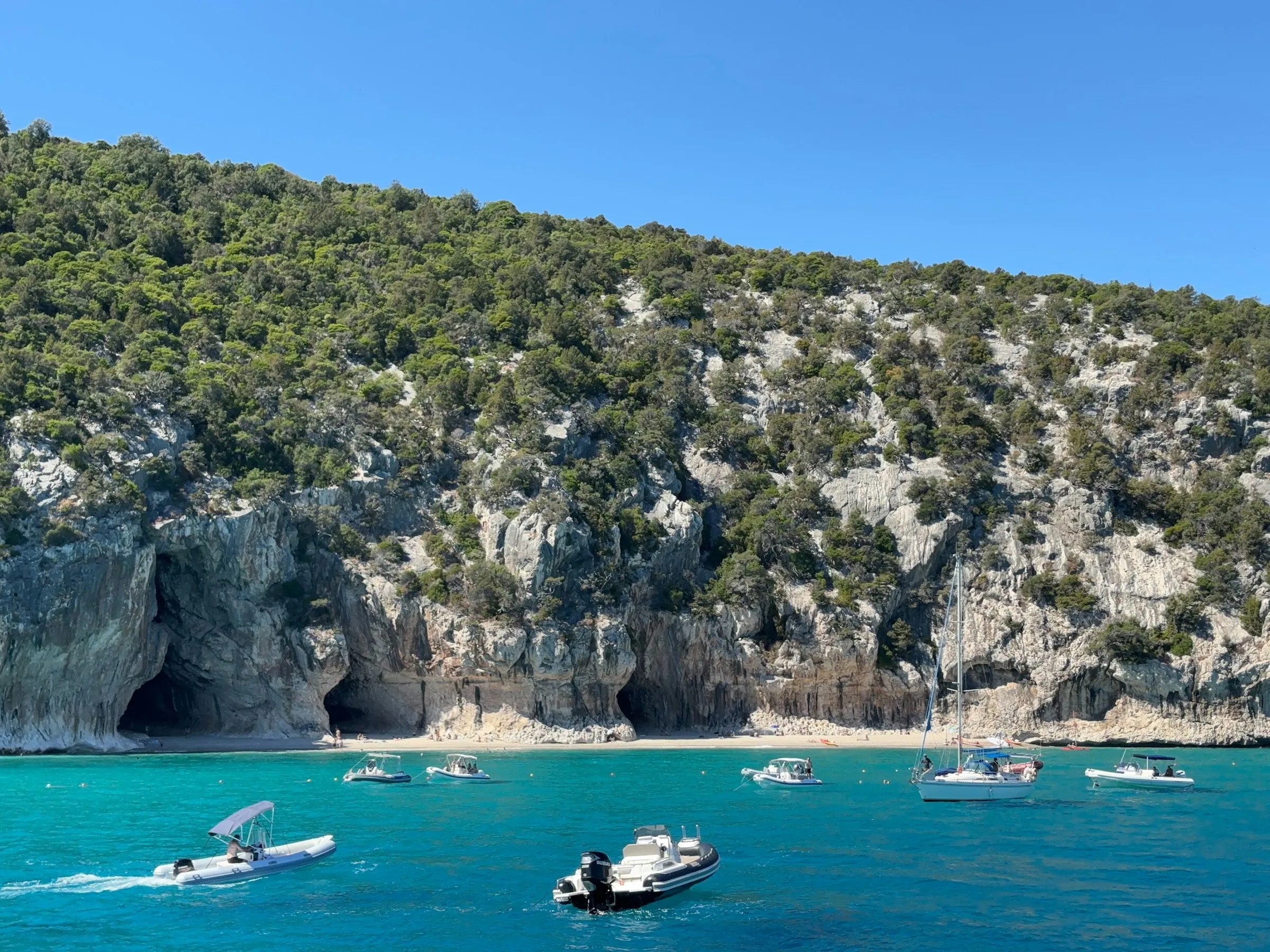 Boats floating on turquoise water near rocky cliffs