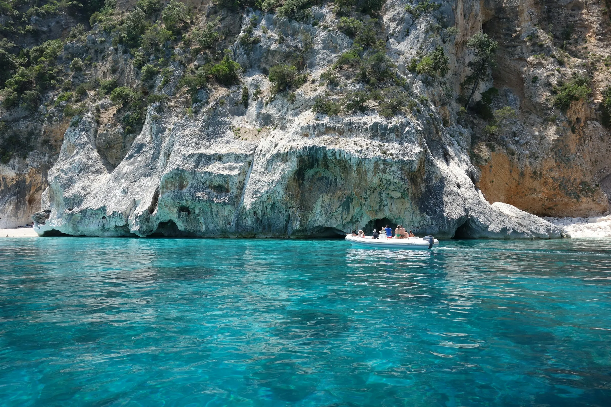 Boat near rocky coastline with clear turquoise water