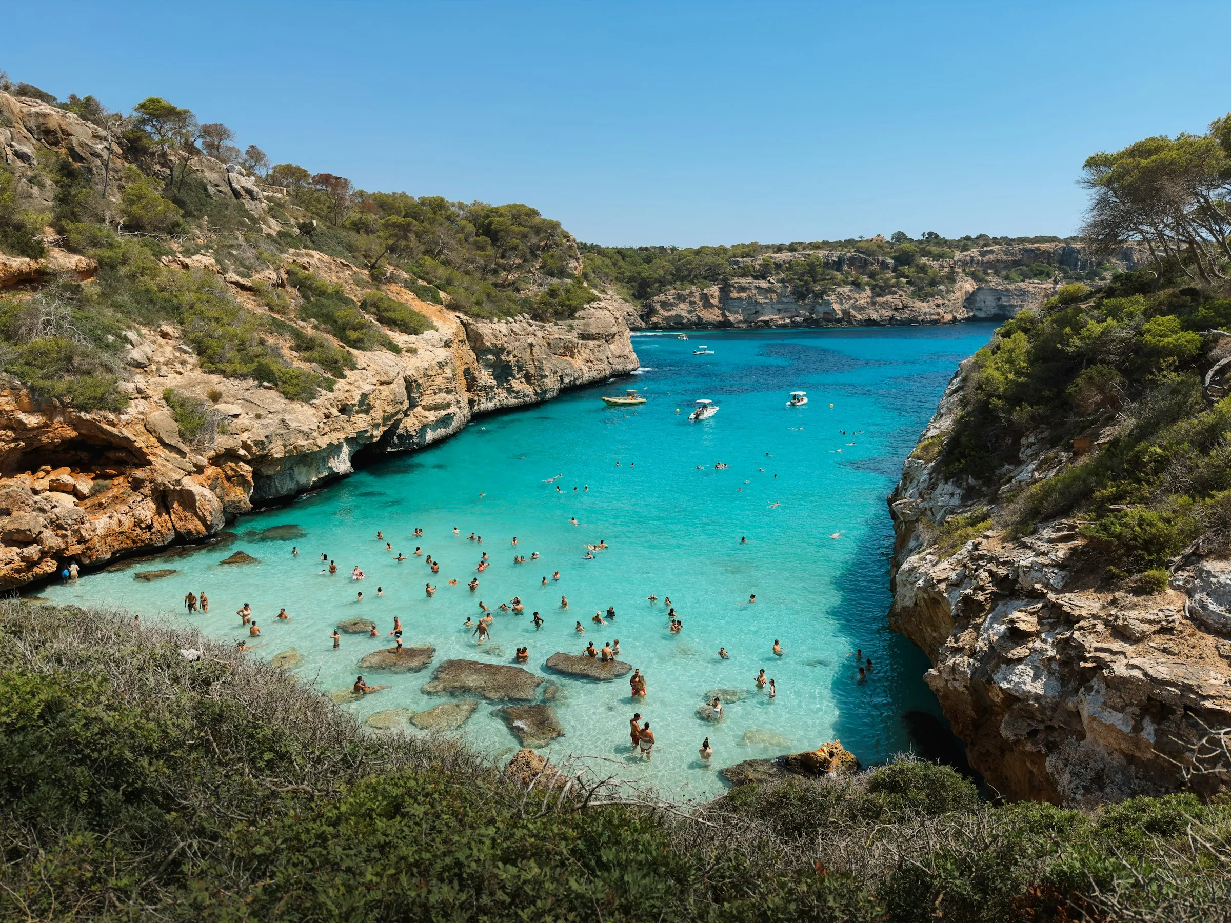 A crowded bay with clear turquoise water and rocky cliffs.