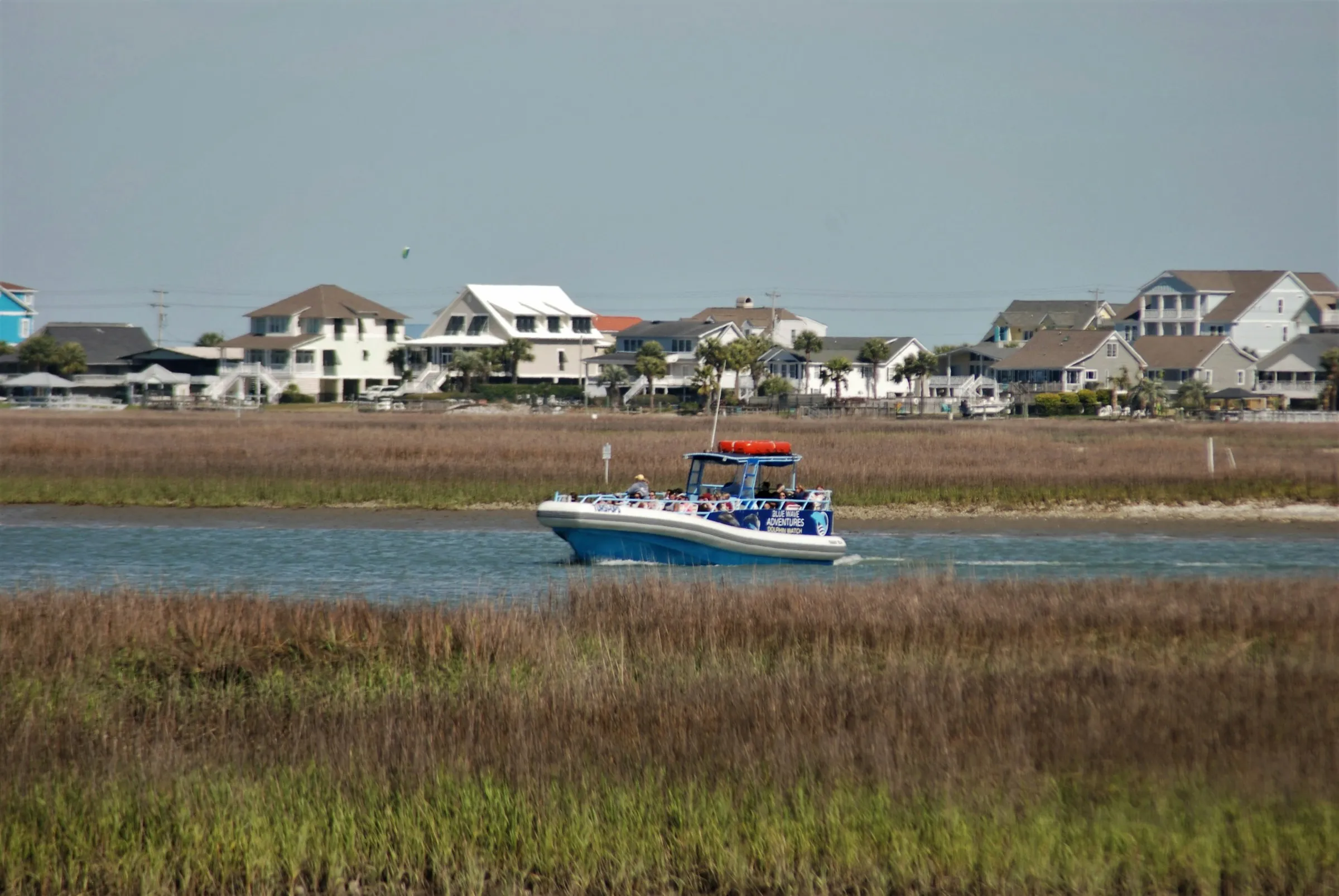 A center-console boat running down a marsh channel with coastal houses behind