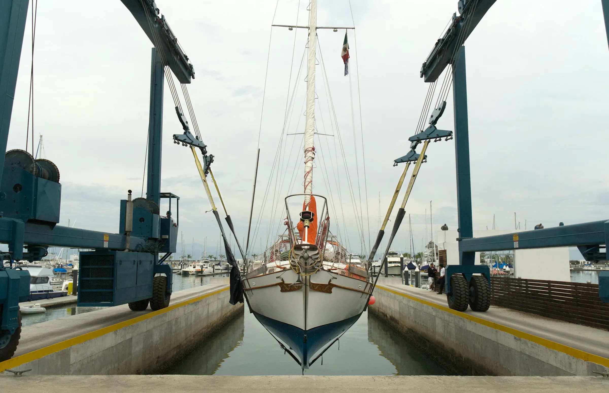 A sailing yacht suspended in a boatyard travelift above the water