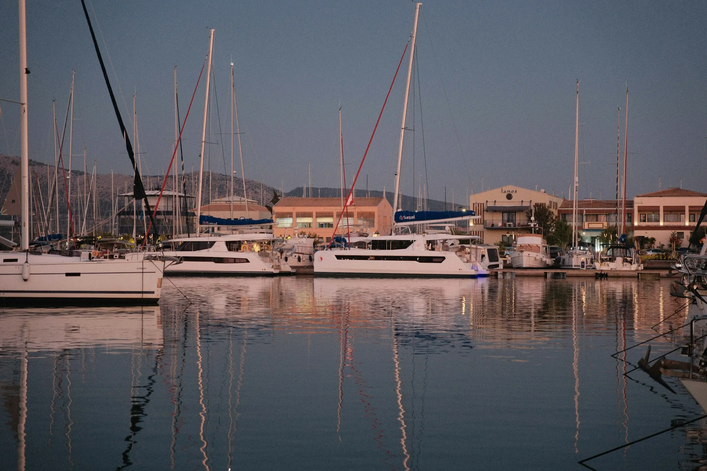 Catamarans and sailboats moored in a still marina at dusk